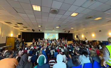 En gruppe mennesker som sitter i et rom med scene og skjerm