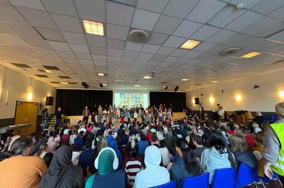 En gruppe mennesker som sitter i et rom med scene og skjerm