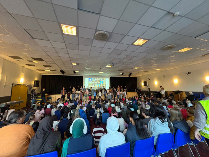 En gruppe mennesker som sitter i et rom med scene og skjerm