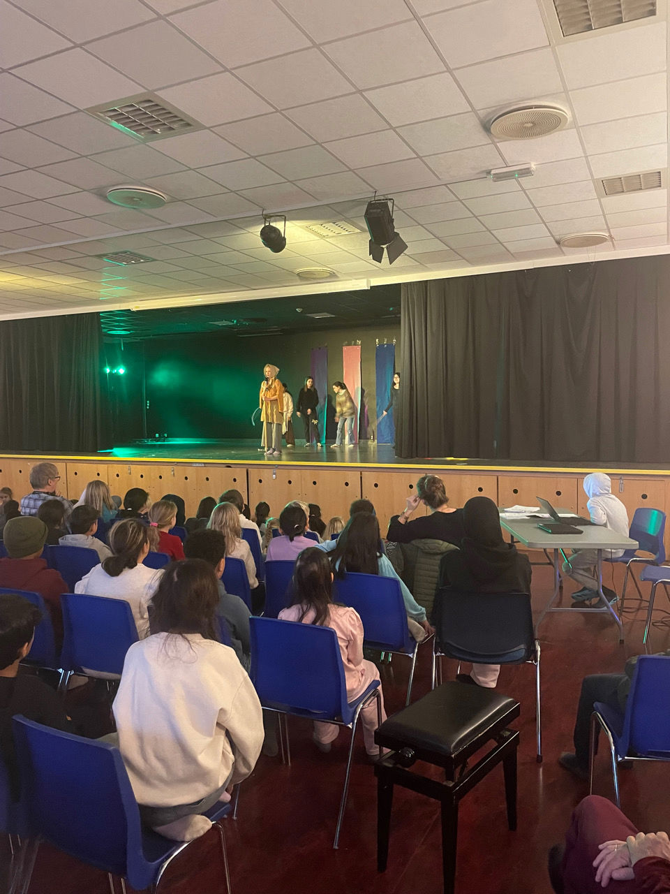 en gruppe mennesker som sitter i et rom med en scene og en person på en scene